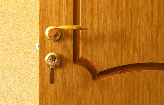 Close-up of wooden interior door with gold-colored curved handle and key inserted into lock. Warm wood grain and polished metal hardware emphasize home security, privacy, access, protection, locking