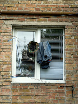 Simple everyday life and poverty concept with work clothes, boot, and camouflage hat hanging to dry on a clothesline outside a window against an old brick wall.
