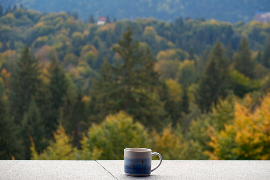 A ceramic mug on a hotel balcony overlooking the beautiful autumn pine forests of Poiana Brasov resort in the Carpathian Mountains, Romania.