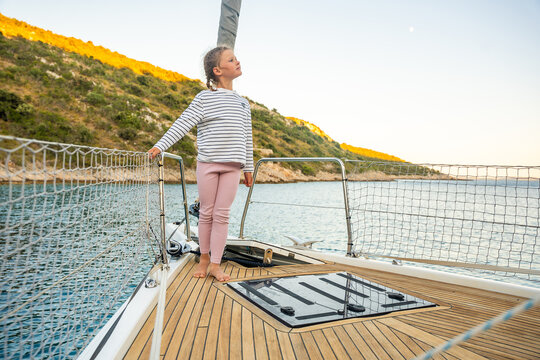 Young girl walking barefoot on sailing yacht deck near Croatian coast. Sailing vacation gives children freedom, confidence and experience of life at sea
