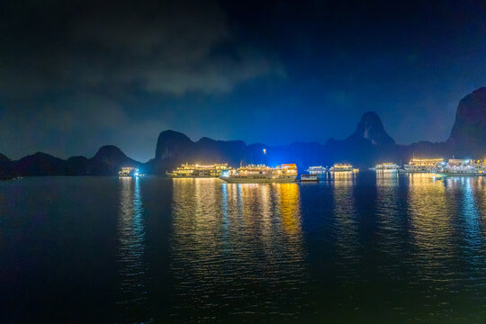 Night view of illuminated cruise ships anchored in Ha Long Bay, Vietnam, at dusk with night clouds and limestone karsts