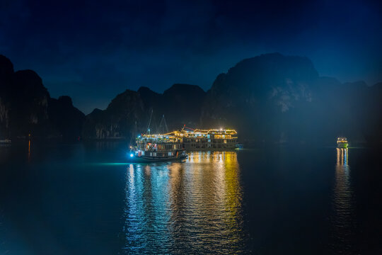 Night view of illuminated cruise ships anchored in Ha Long Bay, Vietnam, at dusk with night clouds and limestone karsts