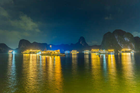 Night view of illuminated cruise ships anchored in Ha Long Bay, Vietnam, at dusk with night clouds and limestone karsts