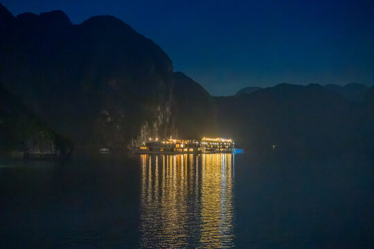 Night view of illuminated cruise ships anchored in Ha Long Bay, Vietnam, at dusk with night clouds and limestone karsts