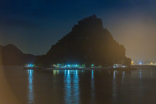 Night view of illuminated cruise ships anchored in Ha Long Bay, Vietnam, at dusk with night clouds and limestone karsts