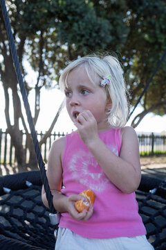Cute Little Blonde Girl Peeling Fresh Tangerine at Outdoor Playground