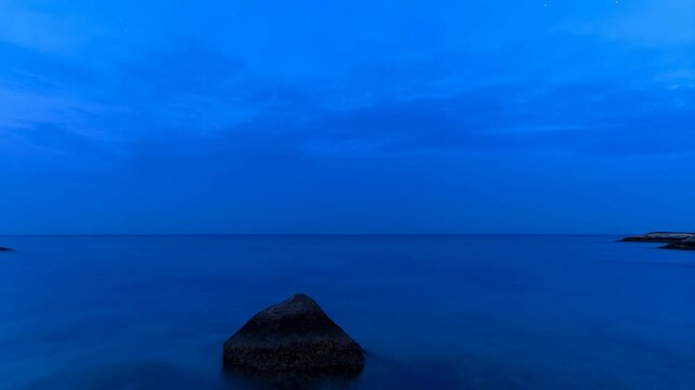 Coastal seascape changes from golden sunset to blue night over calm water