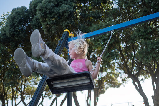 Happy Little Girl Swinging High on Chain Swing at Outdoor Playground