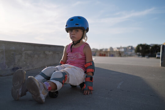 Little Girl in Blue Helmet and Protective Gear Sitting on Penny Board at Skatepark
