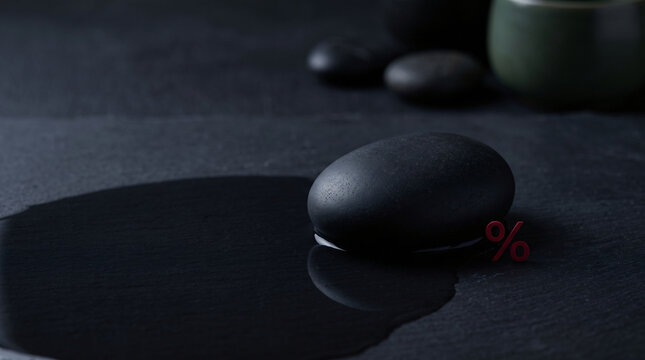Dark, solitary rock rests on calm, black water, creating ripples. Black Friday