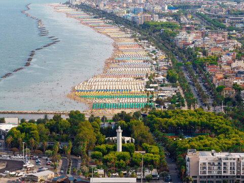 Aerial view of the coastline with rows of colorful beach umbrellas, the port authority lighthouse, and urban buildings in San Benedetto del Tronto, Marche, Italy.