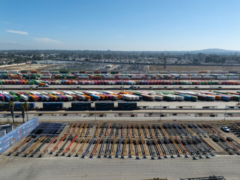 Aerial view of an intermodal rail yard with rows of colorful shipping containers, rail cars, and chassis trailers in the industrial landscape of Carson, California, United States.