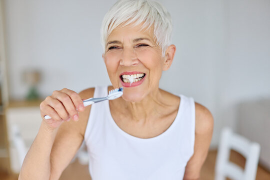 Portrait of an elderly senior woman is cleaning brushing his teeth in front of mirror in bathroom. Dental hygiene, vitality and beauty concepts