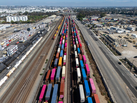 Aerial view of a busy freight train yard filled with colorful shipping containers on multiple parallel tracks in Carson, California, United States.
