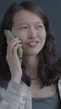 Happy Asian woman speaking on mobile phone smiling on black background. Cellphone communication and people concept.