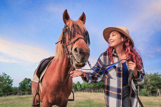 Young woman holding leather reins beside a chestnut horse fitted with decorative bridle fringe outdoors. Equestrian bond concept.