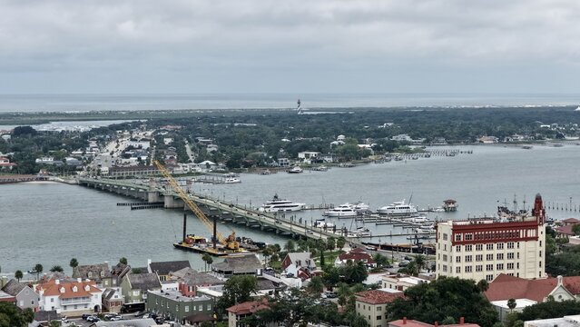 Aerial view of the Bridge of Lions over the Matanzas River with a construction crane, boats at the marina, and the St. Augustine Lighthouse, St. Augustine, Florida, United States.