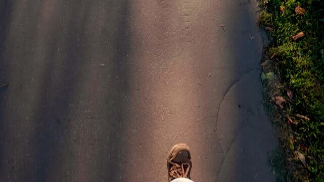 First person view of person walking on asphalt path at sunset