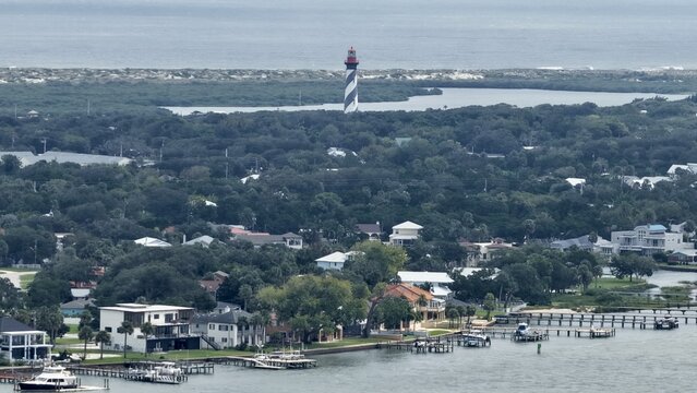 Aerial view of the St. Augustine Lighthouse rising above dense coastal greenery and residential homes along the waterfront in St. Augustine, Florida, United States.