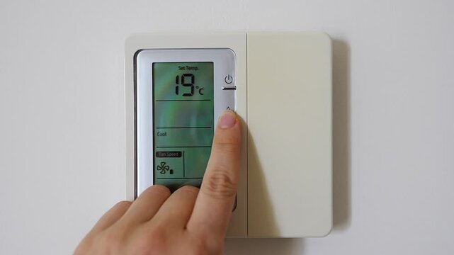 Hand adjusting a digital thermostat set to 22 degrees on a modern wall mounted climate controller. Smart home technology, indoor comfort and energy efficient temperature control.