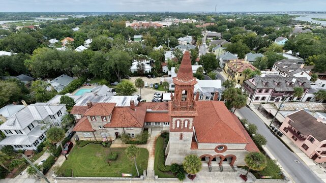 Aerial view of Grace United Methodist Church with its distinctive red-tiled roof and bell tower, surrounded by historic buildings and lush trees in St. Augustine, Florida, United States.