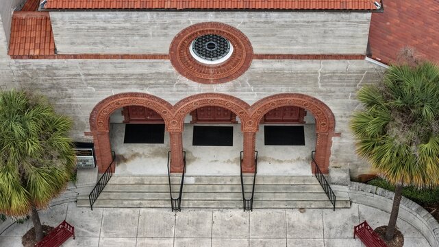 Aerial view of Grace United Methodist Church featuring ornate brick arches, a circular rose window, and palm trees flanking the entrance in St. Augustine, Florida, United States.