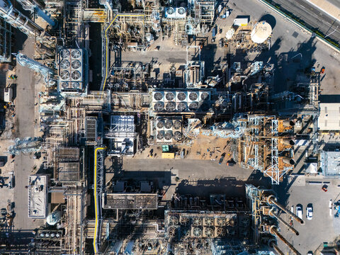 Aerial view of an industrial oil refinery complex featuring complex piping networks, cooling towers, storage tanks, and metallic structures in Carson, California, United States.