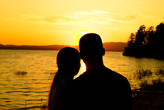 Romantic couple silhouette by lake at golden hour sunset