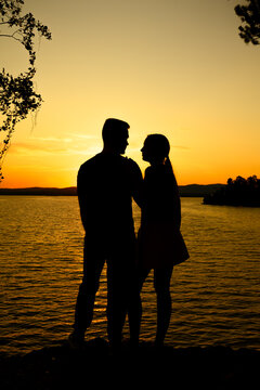 Romantic couple silhouette by lake at golden hour sunset