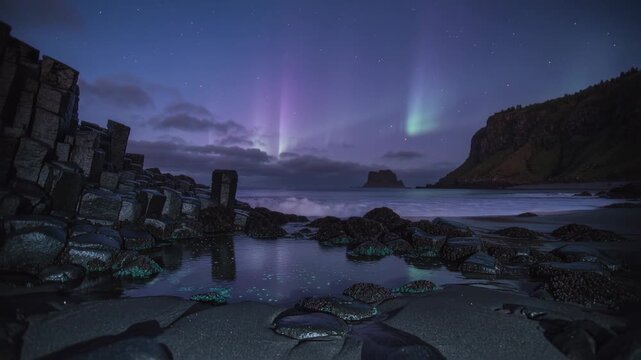 Mirroring tidal pool and rocks showing aurora as surf flowing in, with basalt pillars