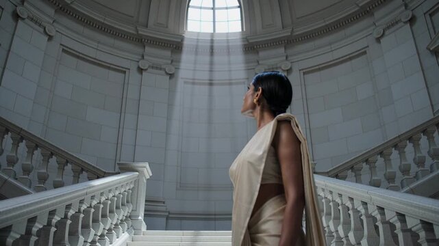 Shaft drawing woman in cream saree, gold earrings lifting head upward at oculus, copy space