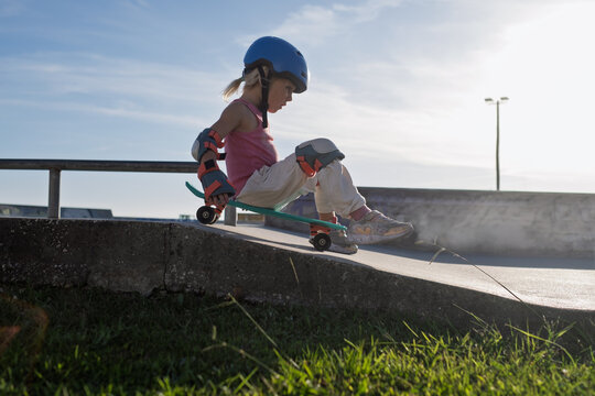  Girl in Helmet and Protective Pads Riding Down Ramp on Penny Board at Skatepark