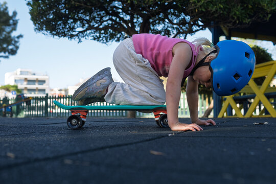 Cute Little Girl in Blue Helmet Sitting on Penny Board at Playground Outdoors