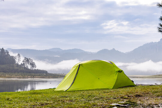Green tent by misty mountain lake for outdoor camping