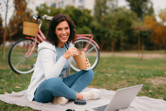 Woman enjoying takeaway food with laptop in autumn park