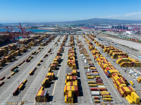 Aerial view of the Port of Long Beach featuring rows of colorful shipping containers, industrial gantry cranes, and logistics infrastructure in Long Beach, California, United States.