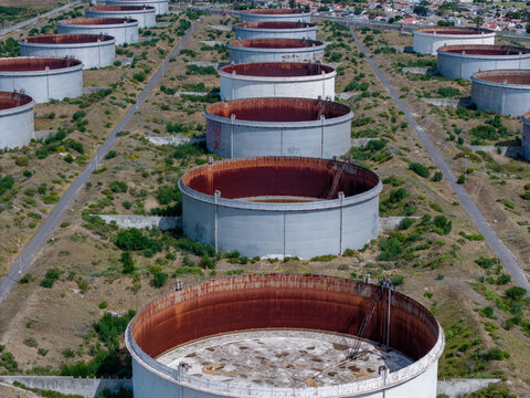 Aerial view of industrial oil storage tanks in Milnerton, featuring large circular steel containers with rusty interiors, surrounded by dry vegetation in Cape Town, Western Cape, South Africa.