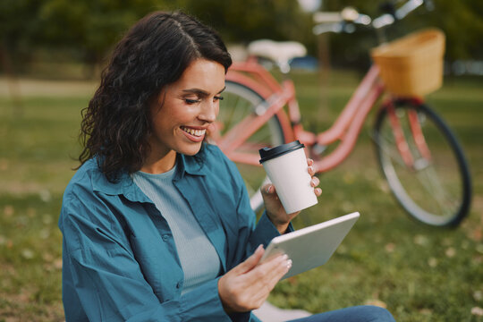 Woman using tablet and drinking coffee beside bicycle