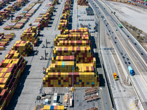 Aerial view of the Port of Long Beach with stacks of colorful shipping containers and a busy highway with vehicles Long Beach, California, United States.