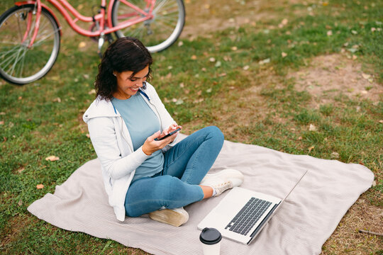 Woman relaxing outdoors working remotely using phone and laptop