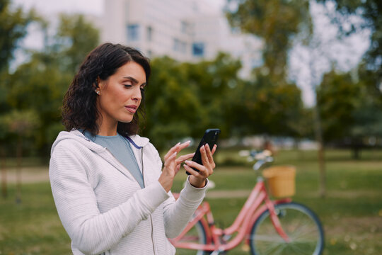 Woman using smartphone in park with bicycle