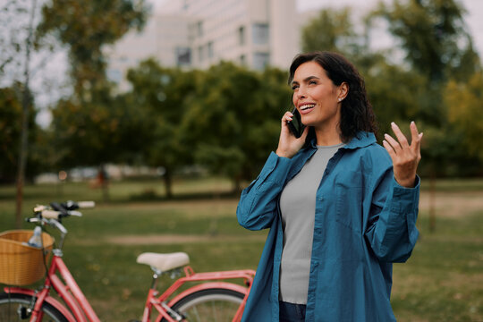 Woman talking on smartphone in park near bicycle