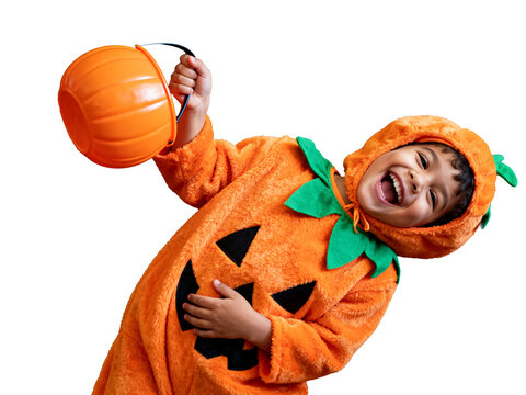 Laughing Halloween child in plush orange pumpkin costume with black jack-o'-lantern smile, holding candy bucket, against dark background