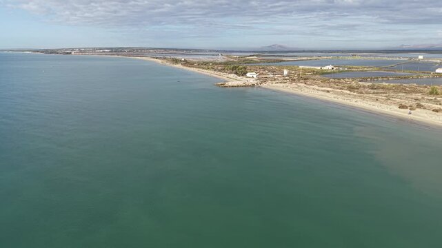 Drone footage flying backward over the coastline and salt flats of Santa Pola, Spain. Scenic view showing ocean shore, water, salt pans, coastal landscape, and natural Mediterranean environment.
