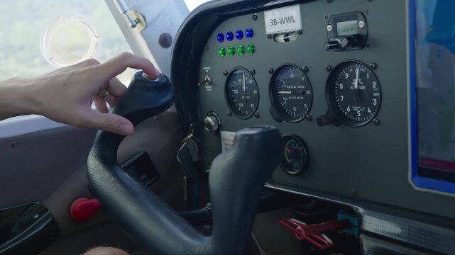 Pilot hand rests on the throttle of a seaplane cockpit in Mauritius, beside an altimeter and vertical speed gauges, the control yoke and green and blue indicator lights. Close up shot