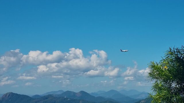 Airplane flying over the hilly landscape of Rio de Janeiro, Brazil, shortly after takeoff, captured from Sugarloaf Mountain against a clear blue sky and lush tropical treetops