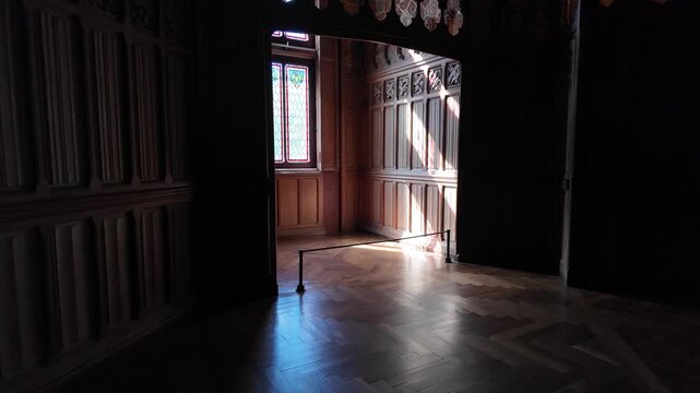 Interior hall at Ch&acirc;teau de Pierrefonds featuring carved wood paneling, a stained glass window, parquet flooring and decorative details