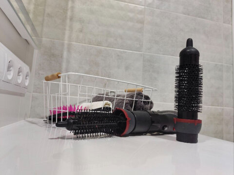Electric hot air brush with interchangeable styling attachments on bathroom counter. Hair care and beauty routine. At-home styling and personal grooming. Cosmetics and wellness