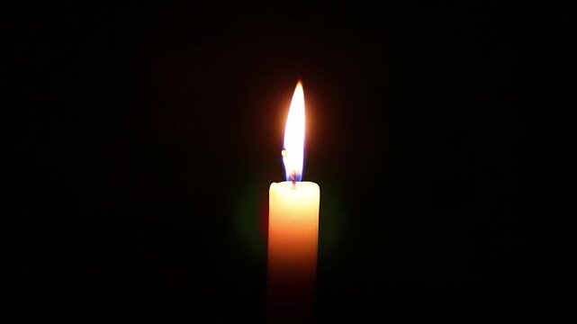 Lit wax taper standing alone dark isolated background. Gentle burning fire flame moving on wind in quiet space. Single candle glowing steadily. romantic setting on black. Thoughtful reflective mood