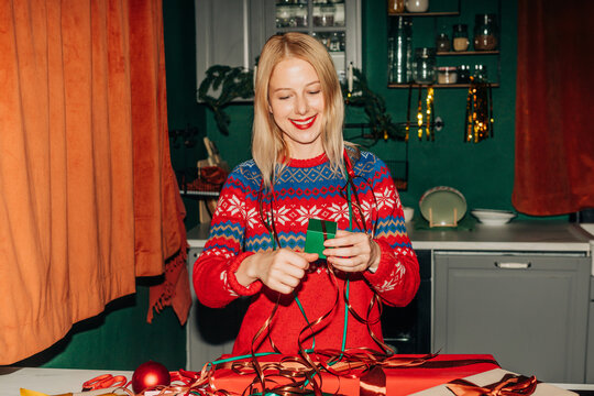 Woman wrap Christmas gift in cozy kitchen at home